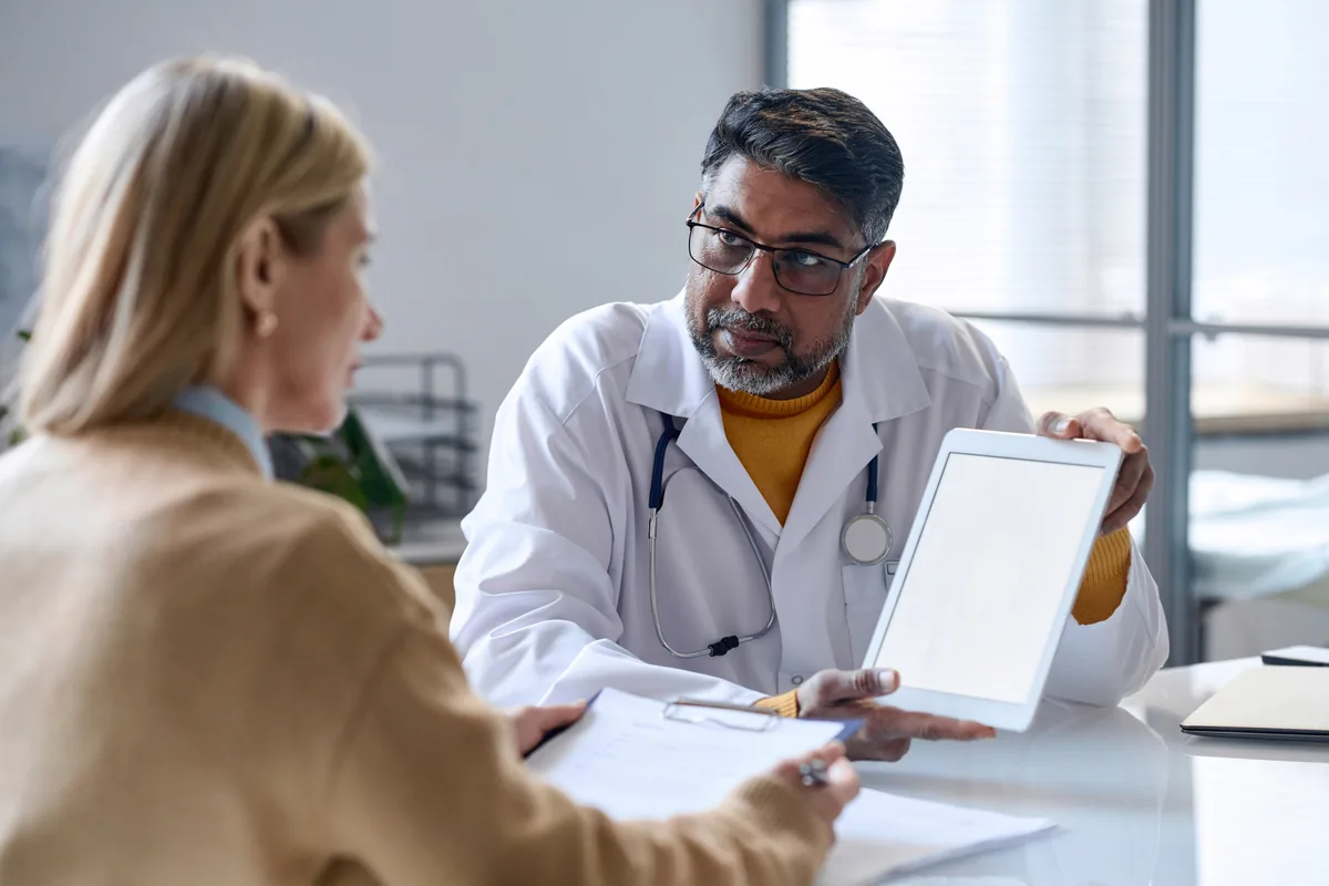 Bir hekim, karşısındaki kadına tablet ekranından bilgi gösteriyor